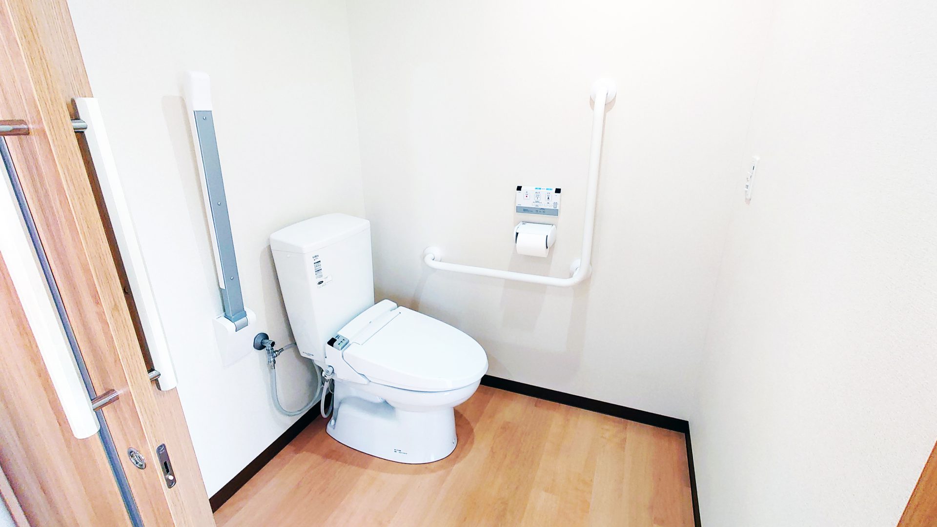 介護施設のトイレ。温水洗浄便座と壁付け手洗い器を備えた清潔な空間。